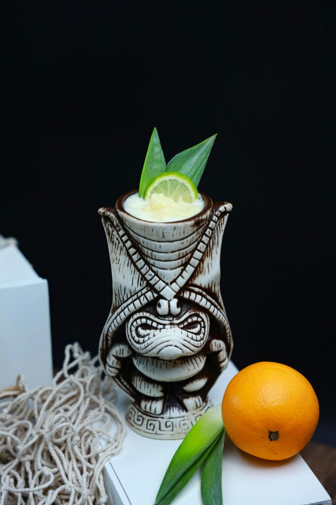 Tropical drink served in a tiki mug with citrus garnish and fresh orange on dark background.